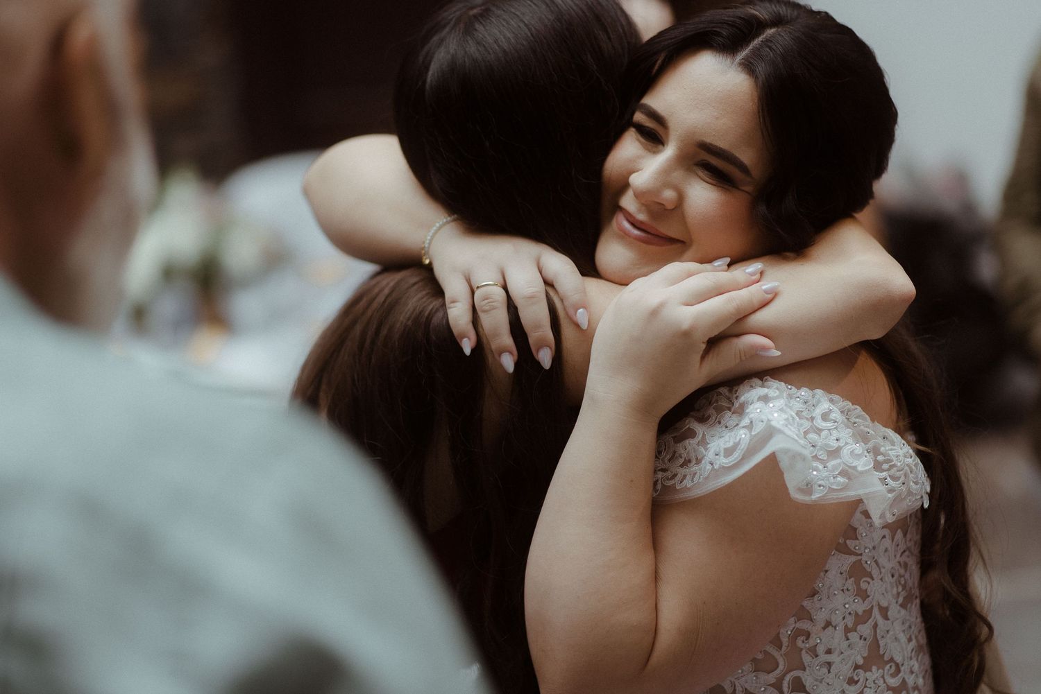 People share an emotional embrace at a wedding ceremony while wearing white lace.