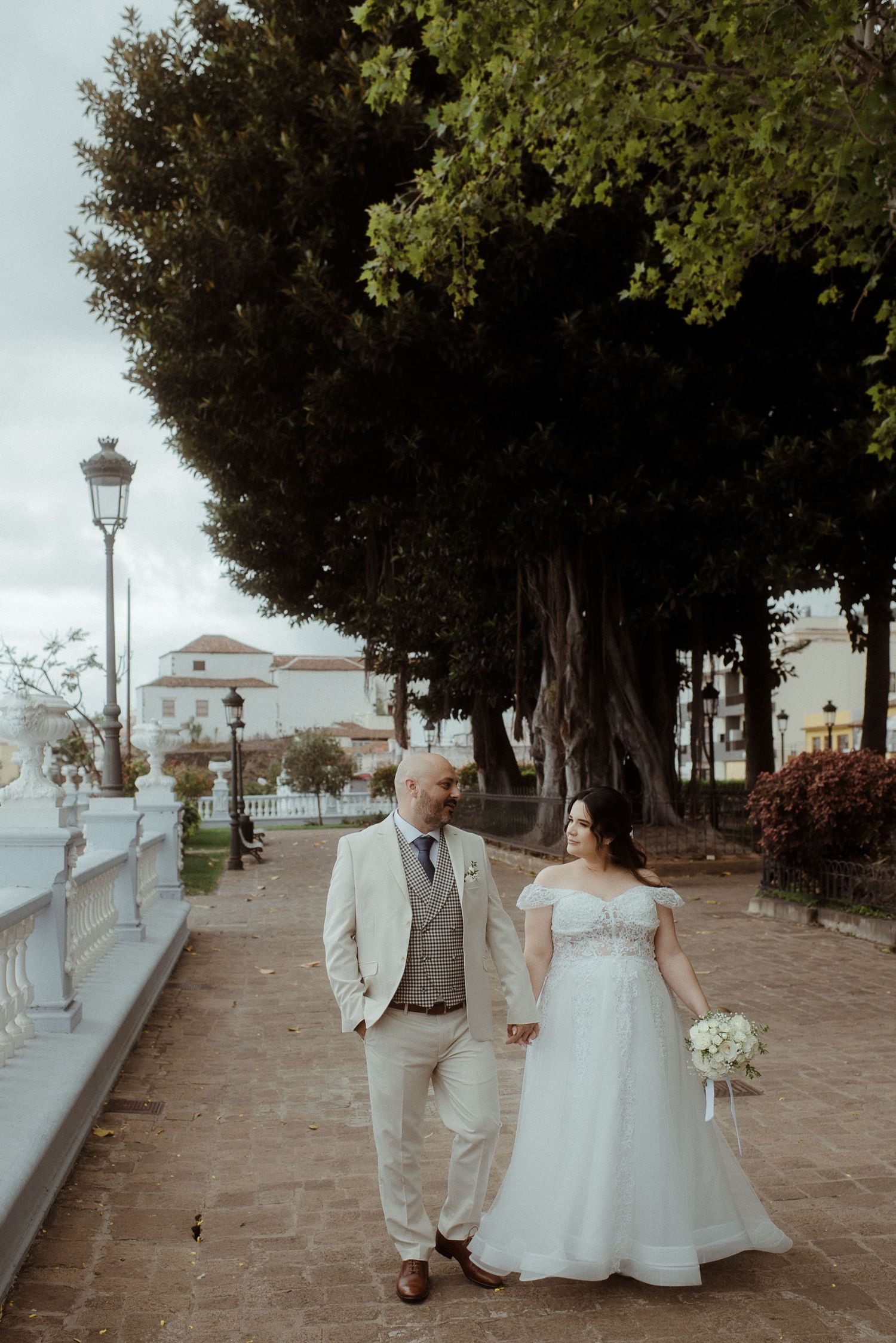 A romantic stroll along a Mediterranean promenade lined with lanterns and trees during a wedding celebration.