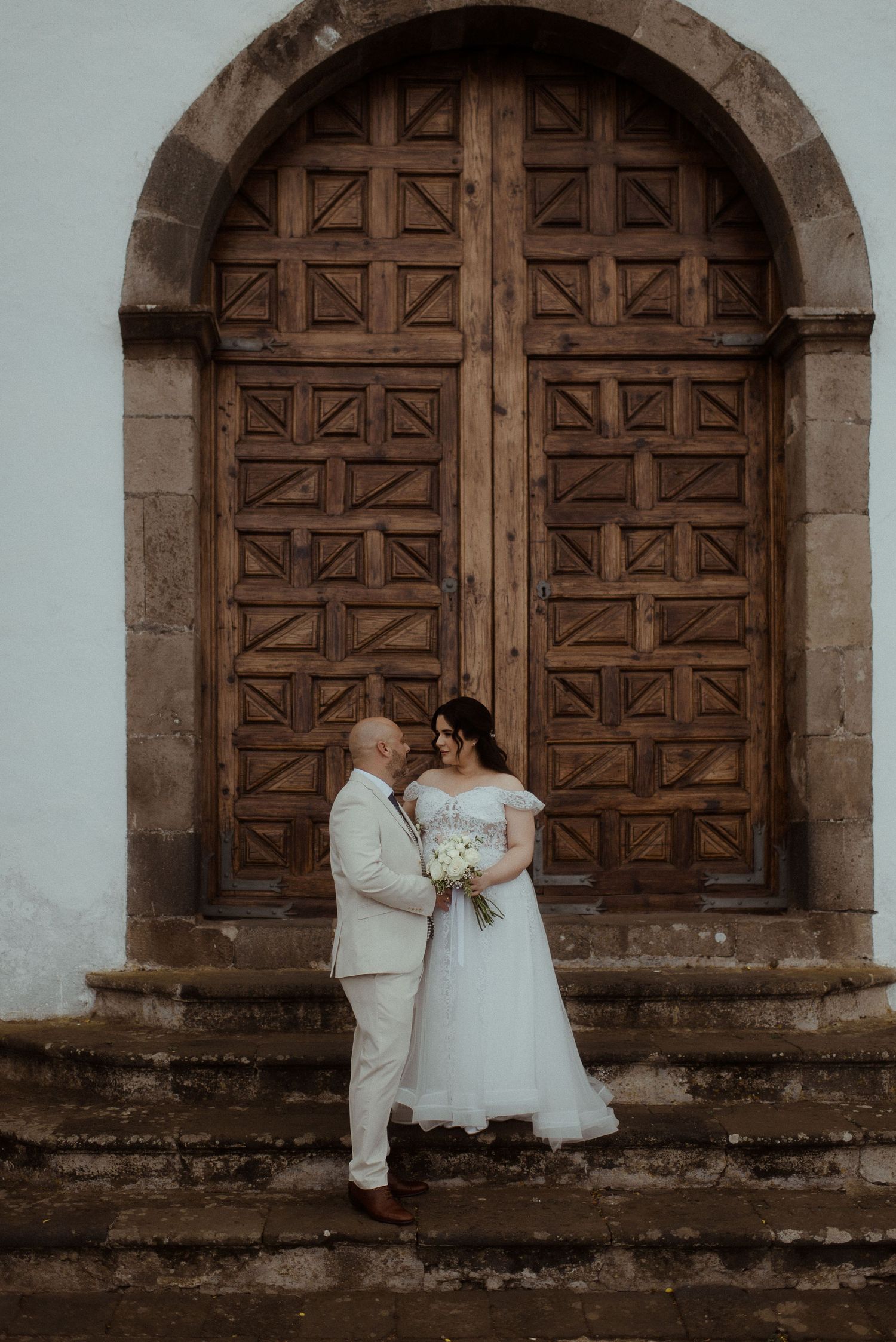 A wedding couple standing before a grand wooden door on stone steps of a historic building.