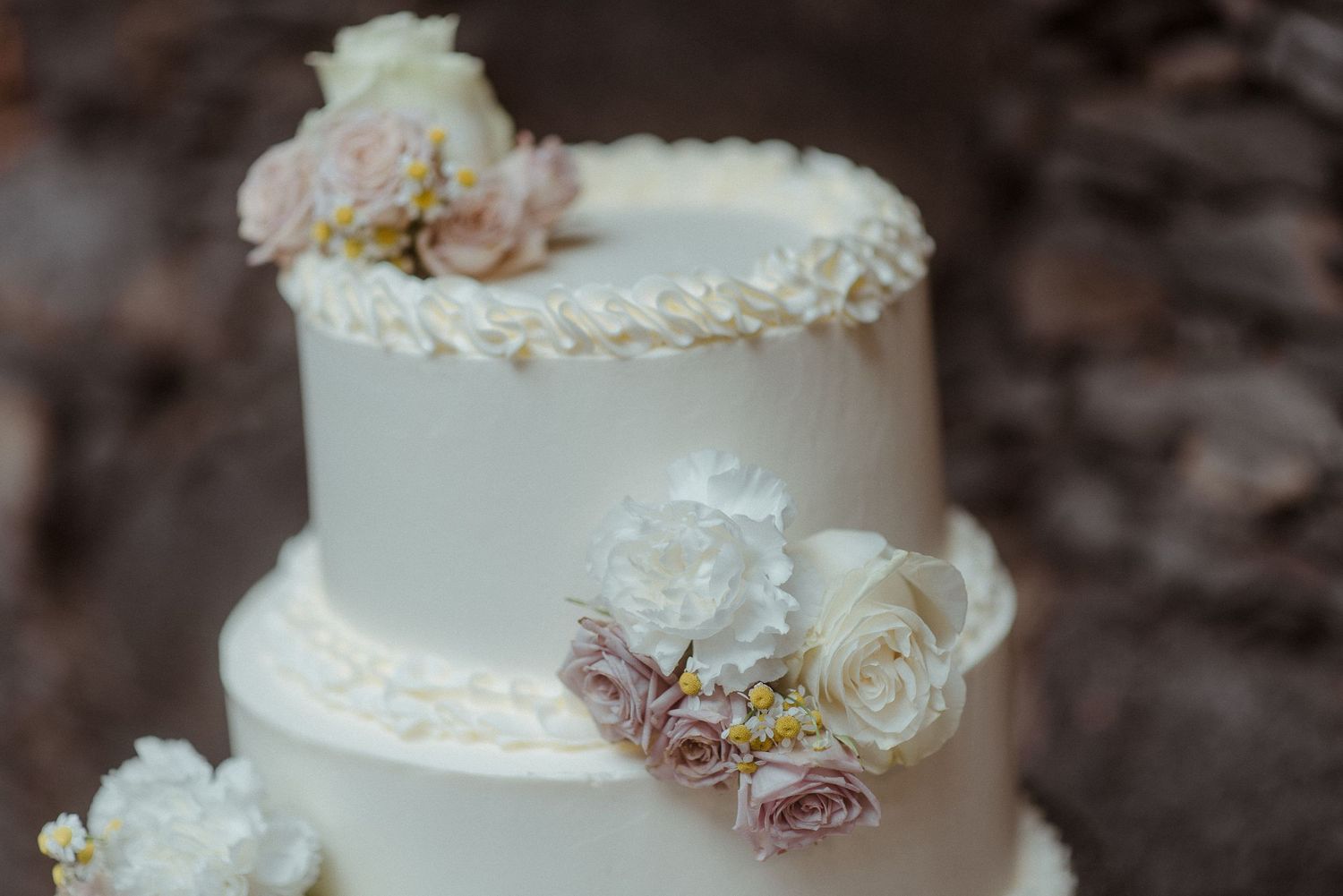 Elegant white tiered wedding cake decorated with fresh pink and ivory roses and delicate lace details.