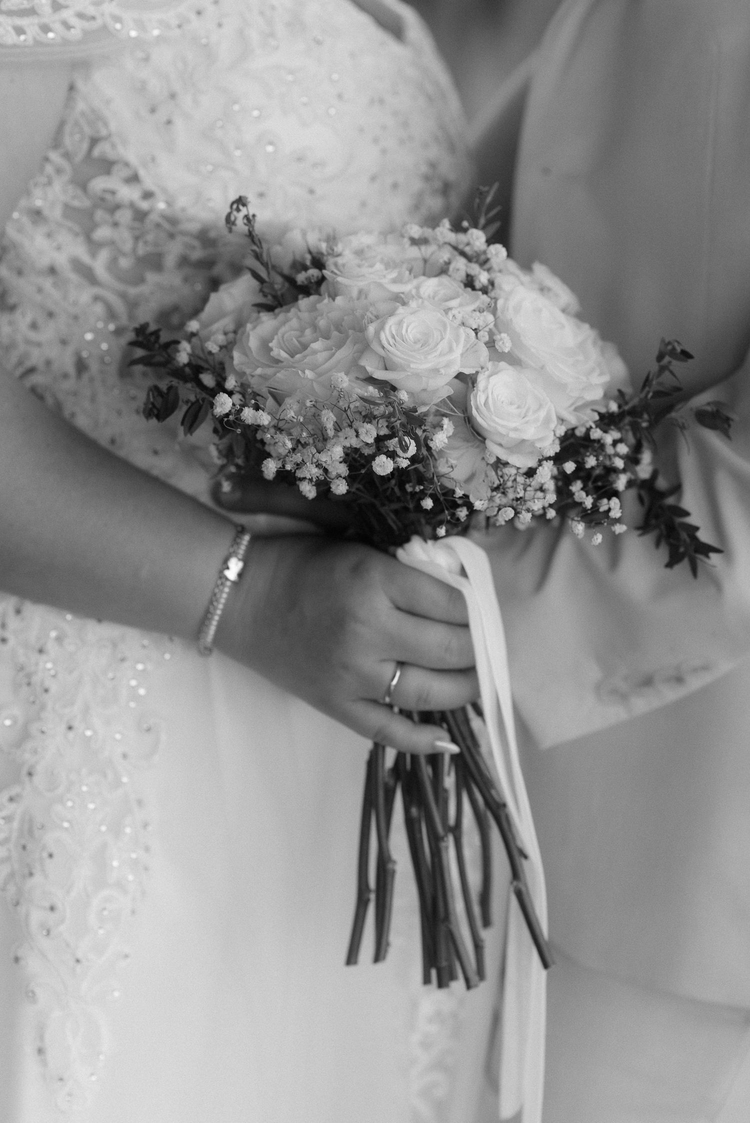 Black and white close-up of a bridal bouquet with roses and delicate flowers tied with ribbon.