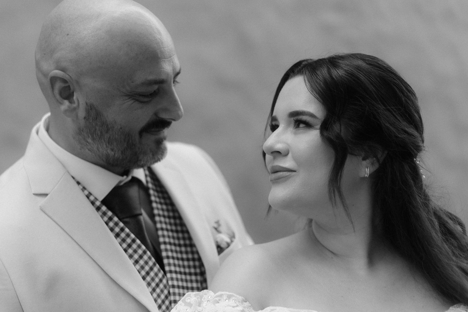 Black and white portrait photo showing a lovely wedding moment between a couple looking at each other outdoors.