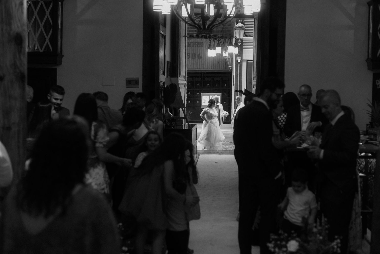 A black and white photo of guests mingling in an elegant hallway during an evening event or reception.