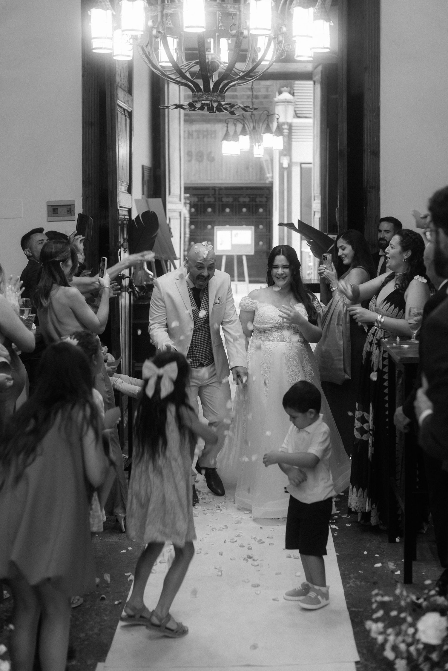 Wedding celebration with guests lining aisle throwing petals while couple walks down decorated indoor venue.