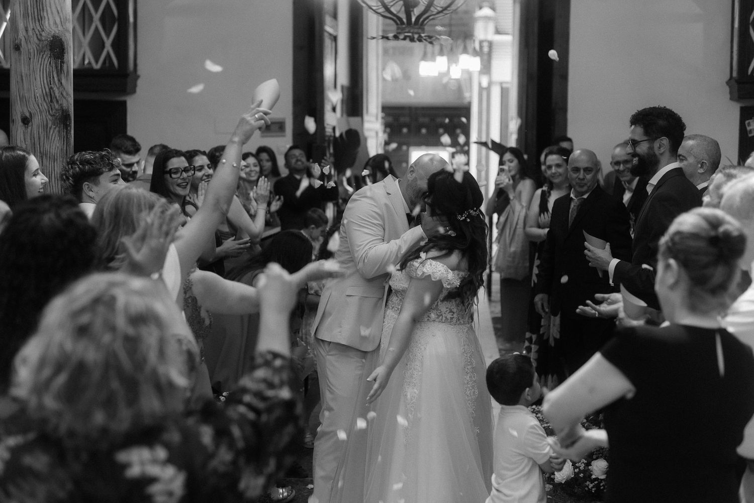 A bride and groom share their first kiss at a wedding ceremony while guests throw confetti in a church.