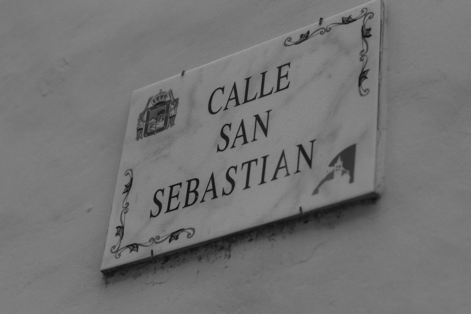 Black and white street sign reading Calle San Sebastian with decorative elements on a white wall.