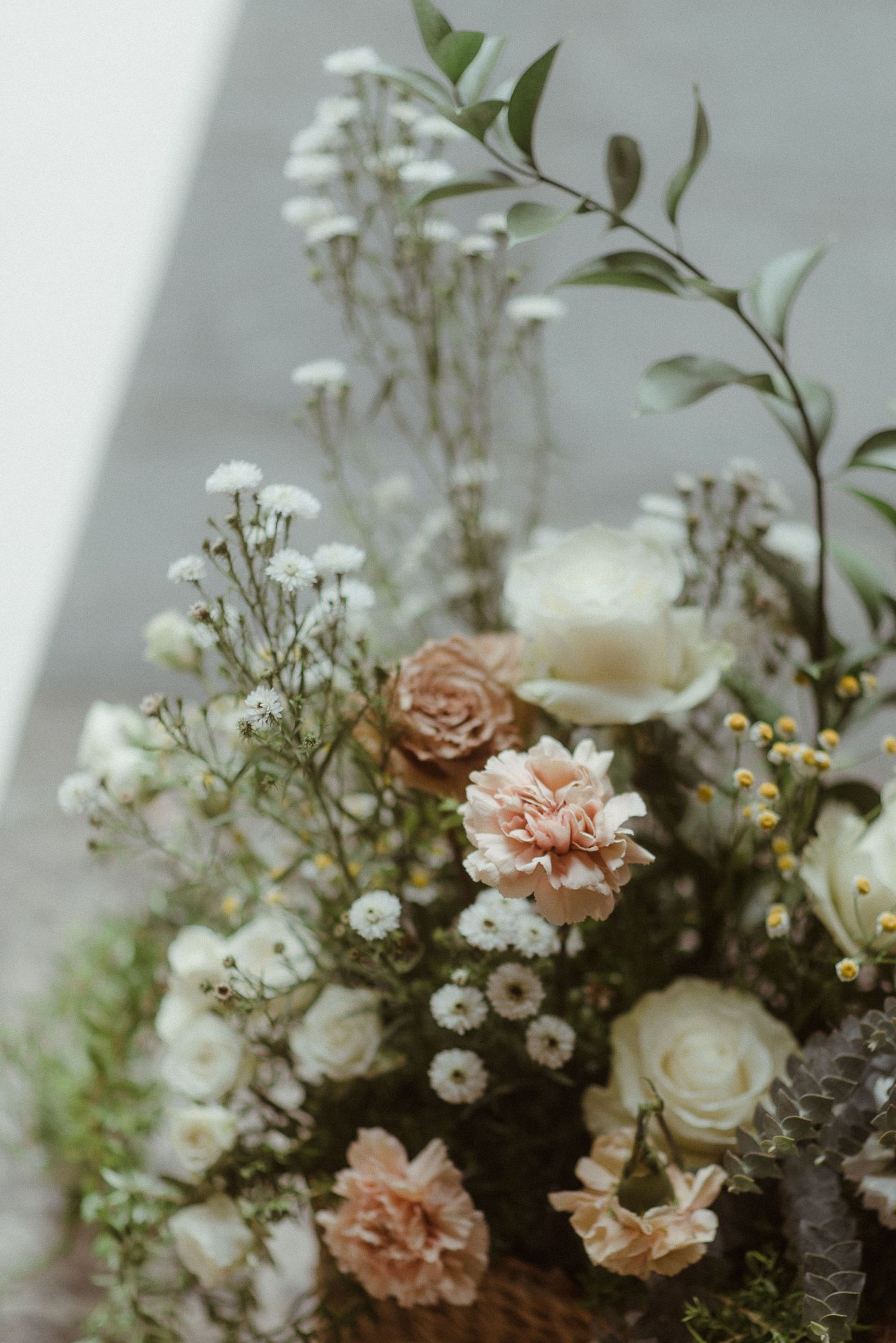 Delicate floral arrangement featuring pale pink carnations, white roses and baby's breath against a soft grey background.
