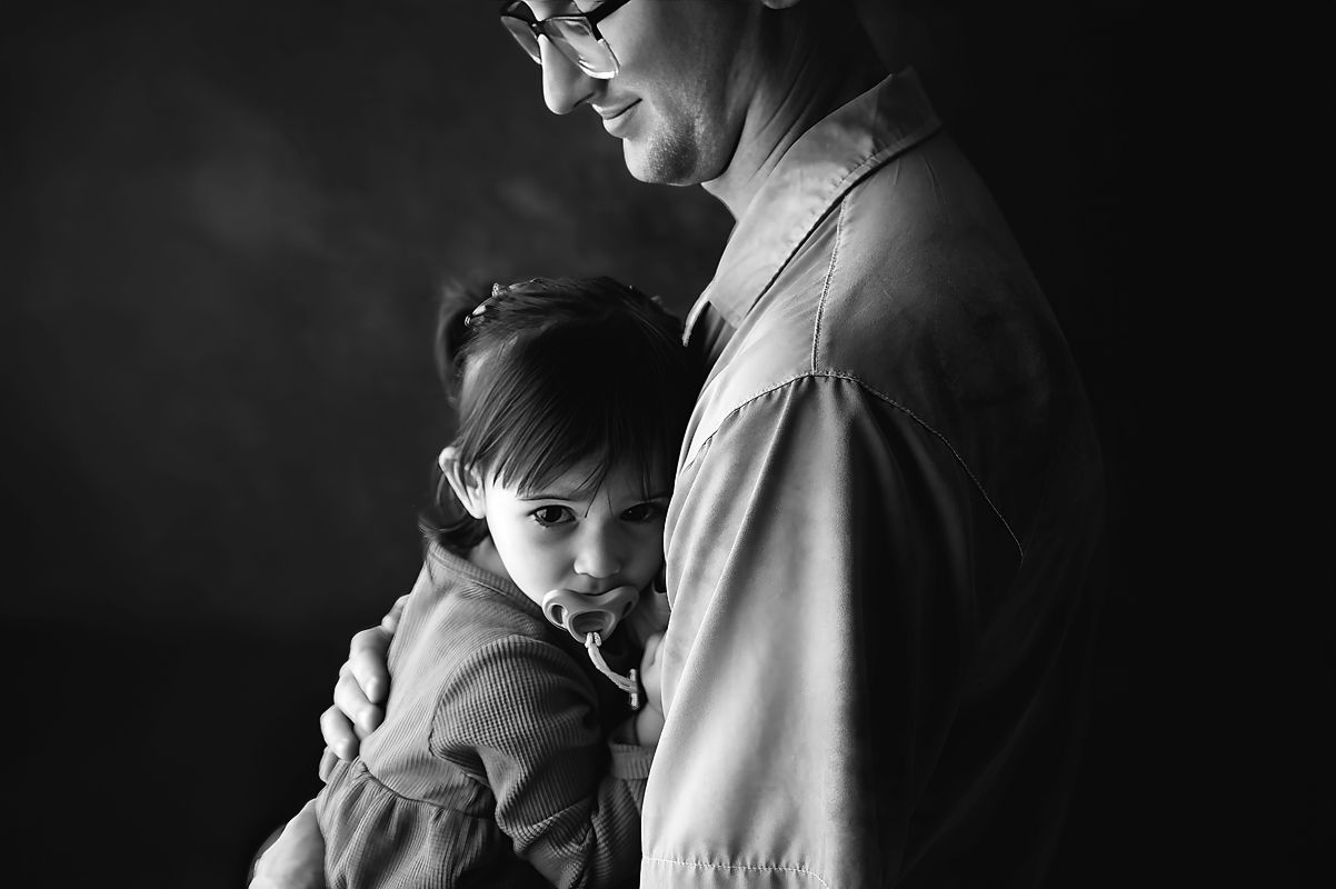 A tender black and white portrait of a dad and child embracing in a gentle hug in the best father's day gift you can give him - portraits.