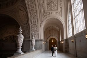 Wide shot of couple looking out the window of 4th floor in San Francisco City Hall on their wedding day.