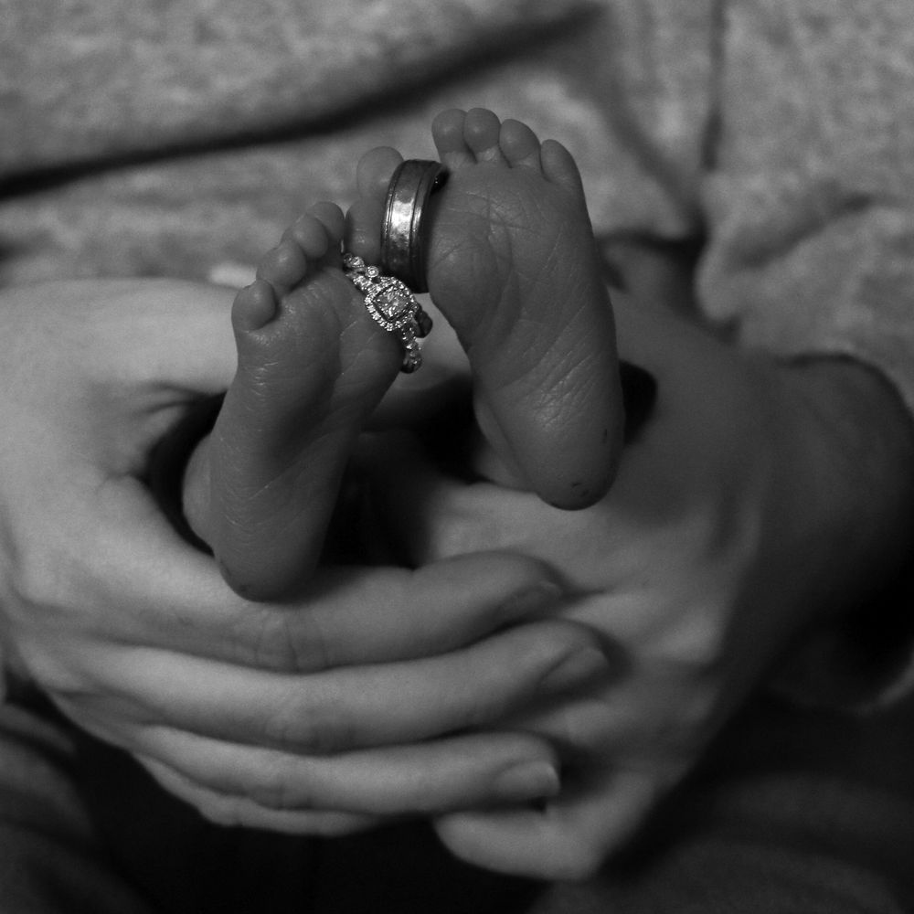 Artistic black and white image of newborn’s feet wearing parents’ wedding rings during Eastern Washington session