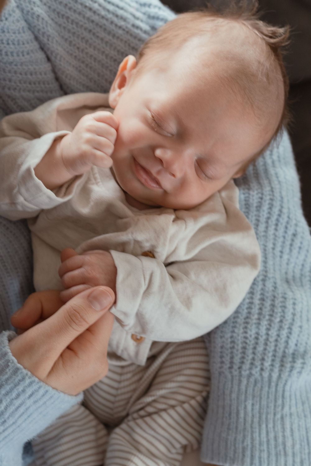 Close-up of smiling newborn lying against parent’s chest during cozy in-home lifestyle session