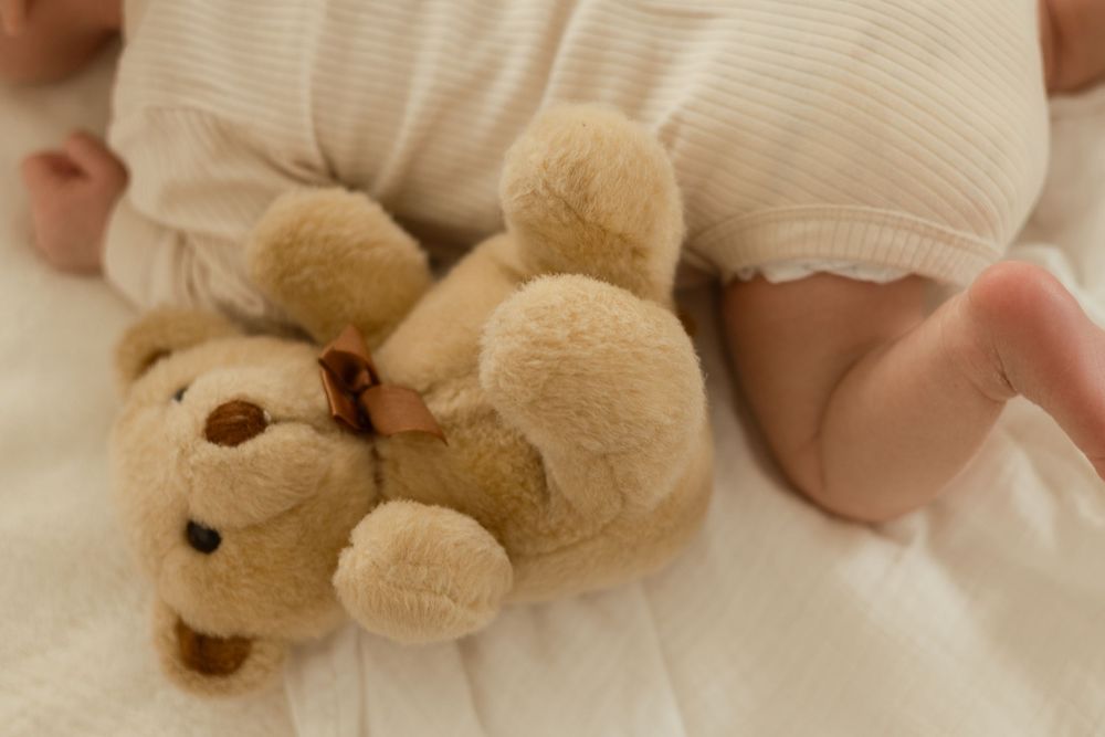 Newborn lying on bed with plush bear during in-home lifestyle session in Pasco WA