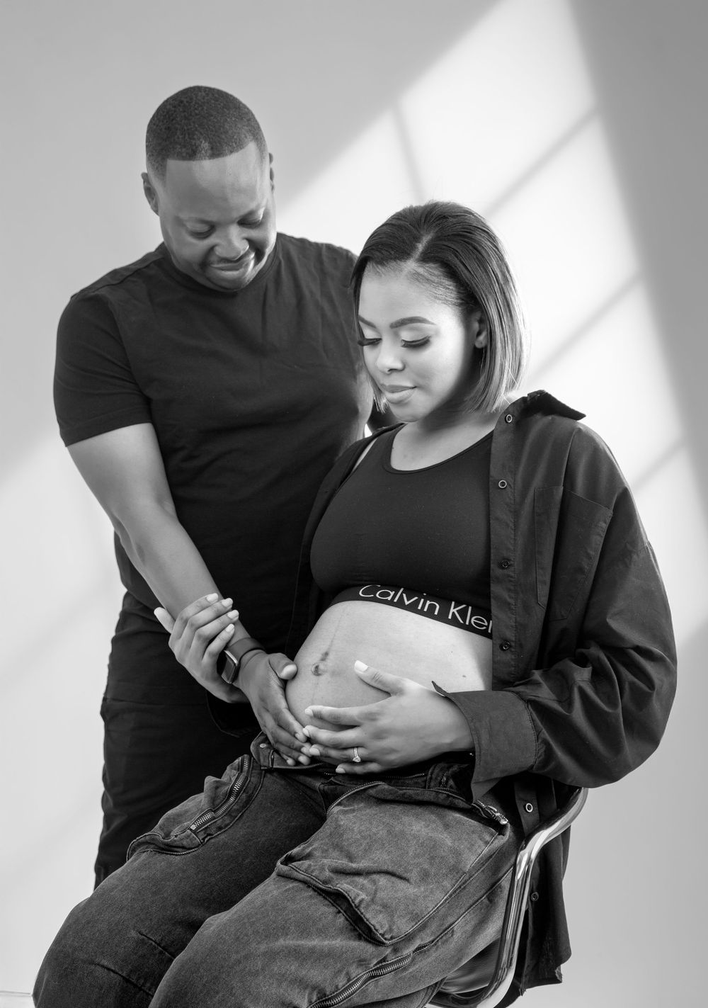 An intimate black and white maternity photo showing a couple embracing with hands on pregnant belly.