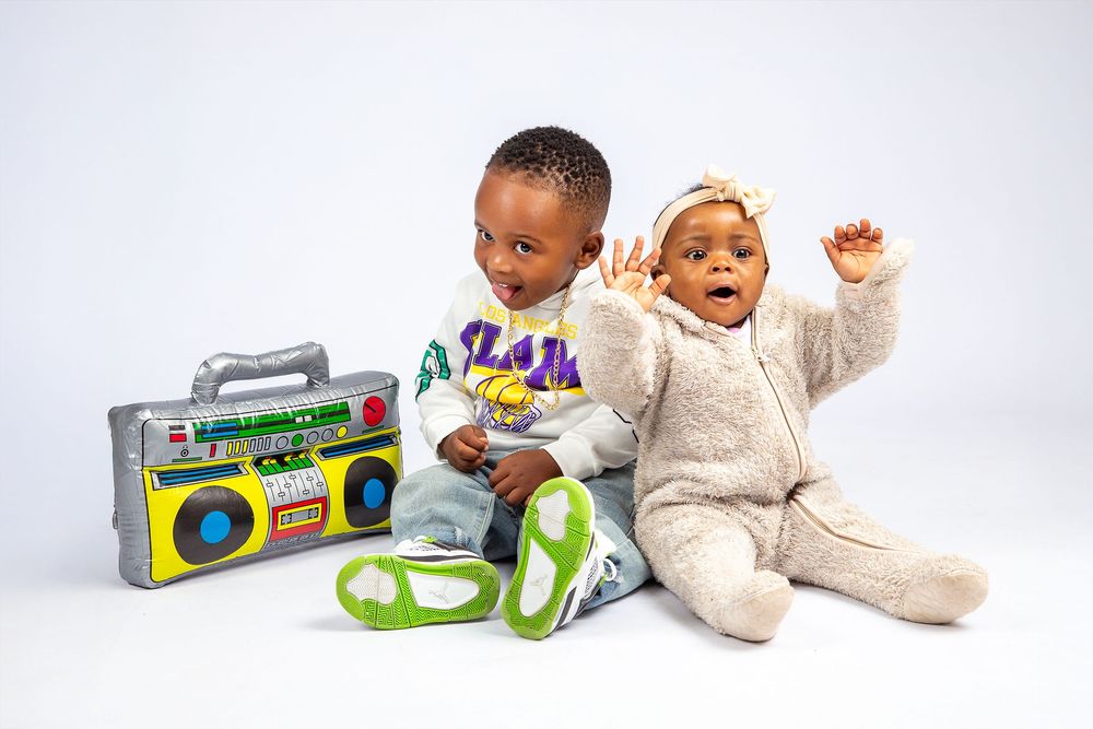 Two children sit together with colorful toy boombox and headphones against white background.