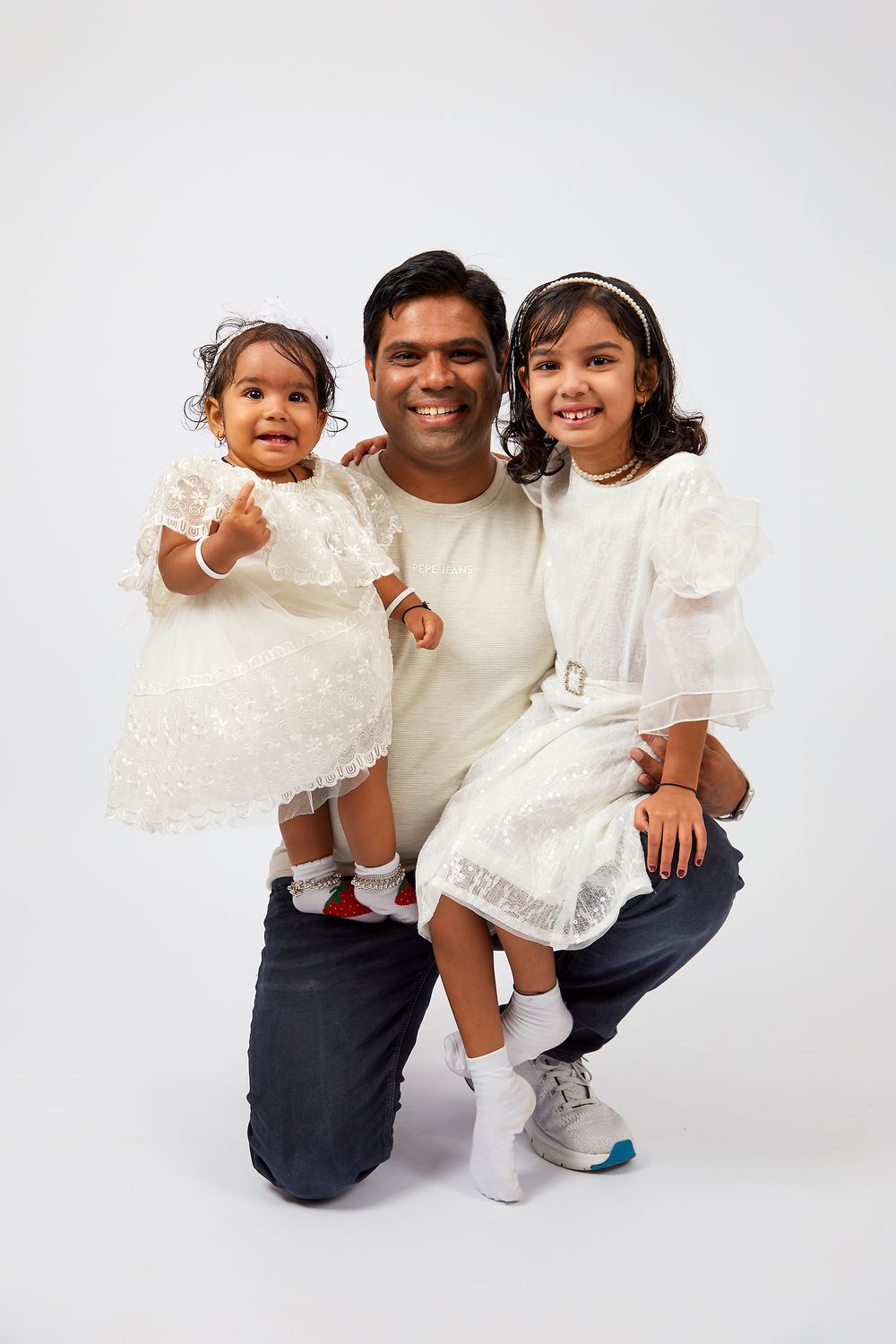 A family in coordinating white tops and navy pants pose together against a white studio background for professional photos.
