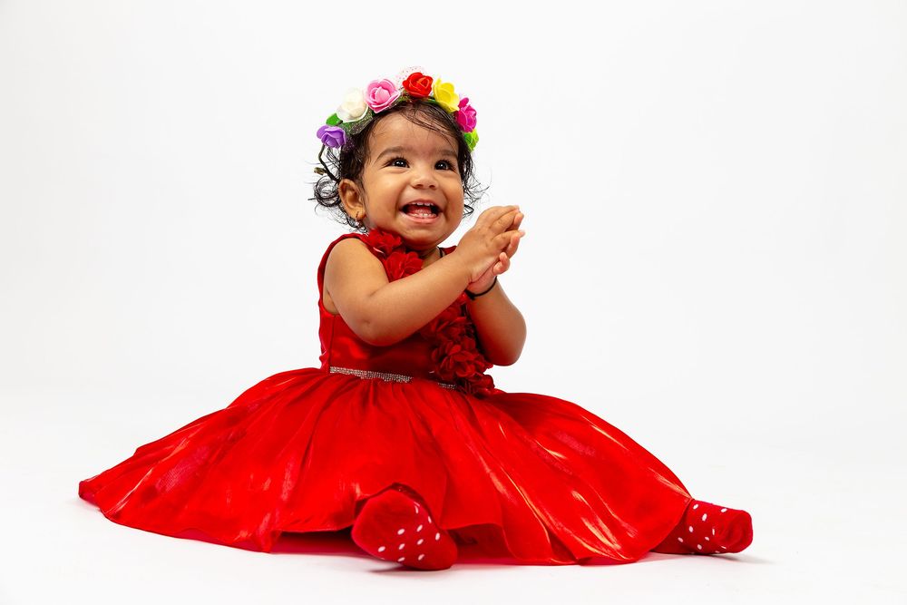Baby in a red dress giggles and plays in a series of progressive poses against a white background.