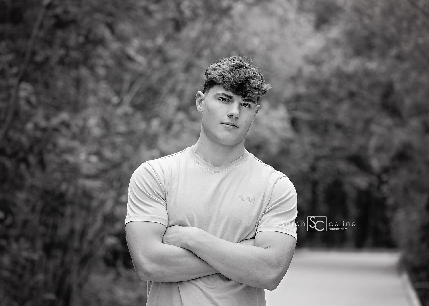 An individual in a white t-shirt poses outdoors with a blurred natural background.