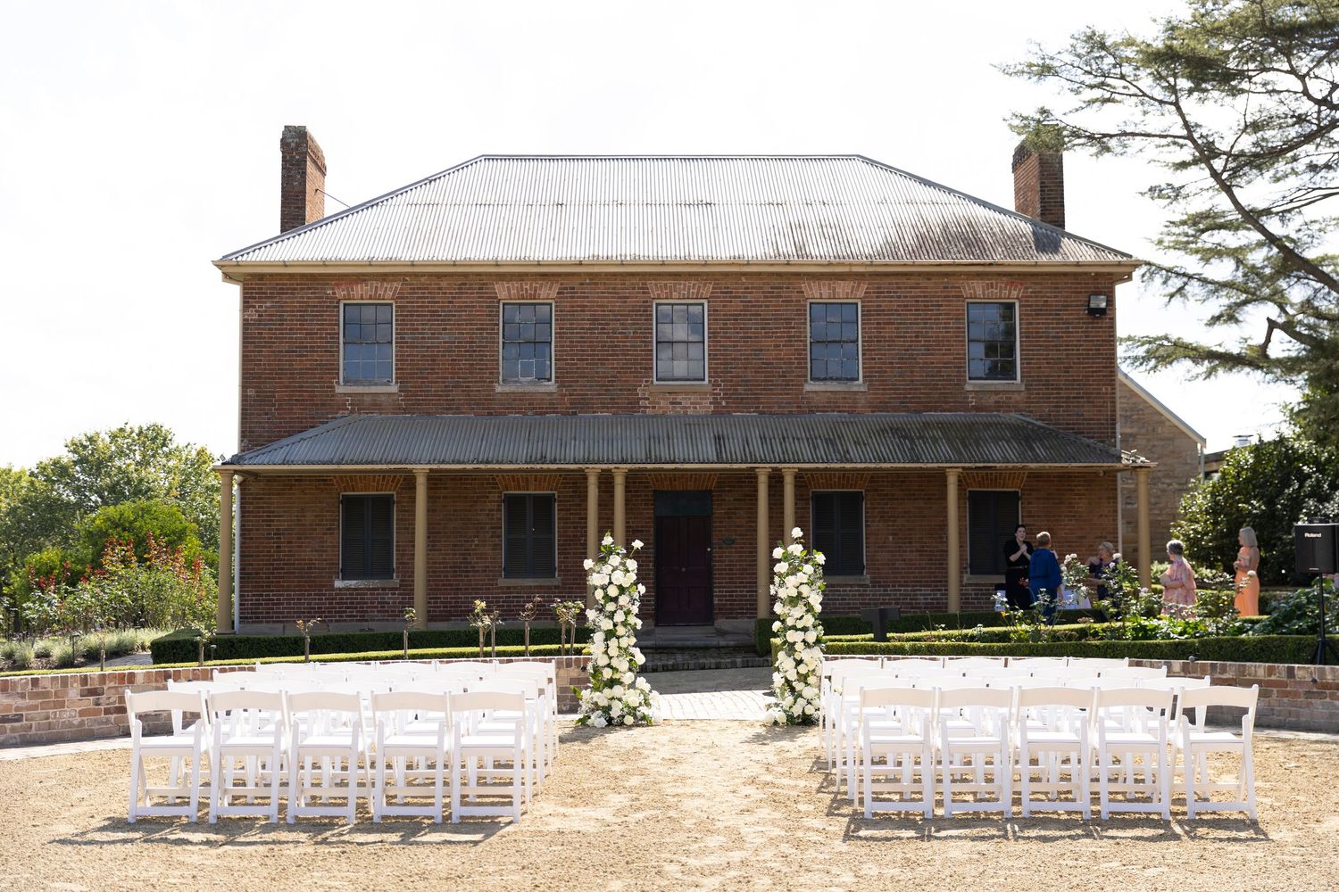 Historic red brick mansion with white pillars set up for an outdoor wedding ceremony with rows of white chairs on the lawn.