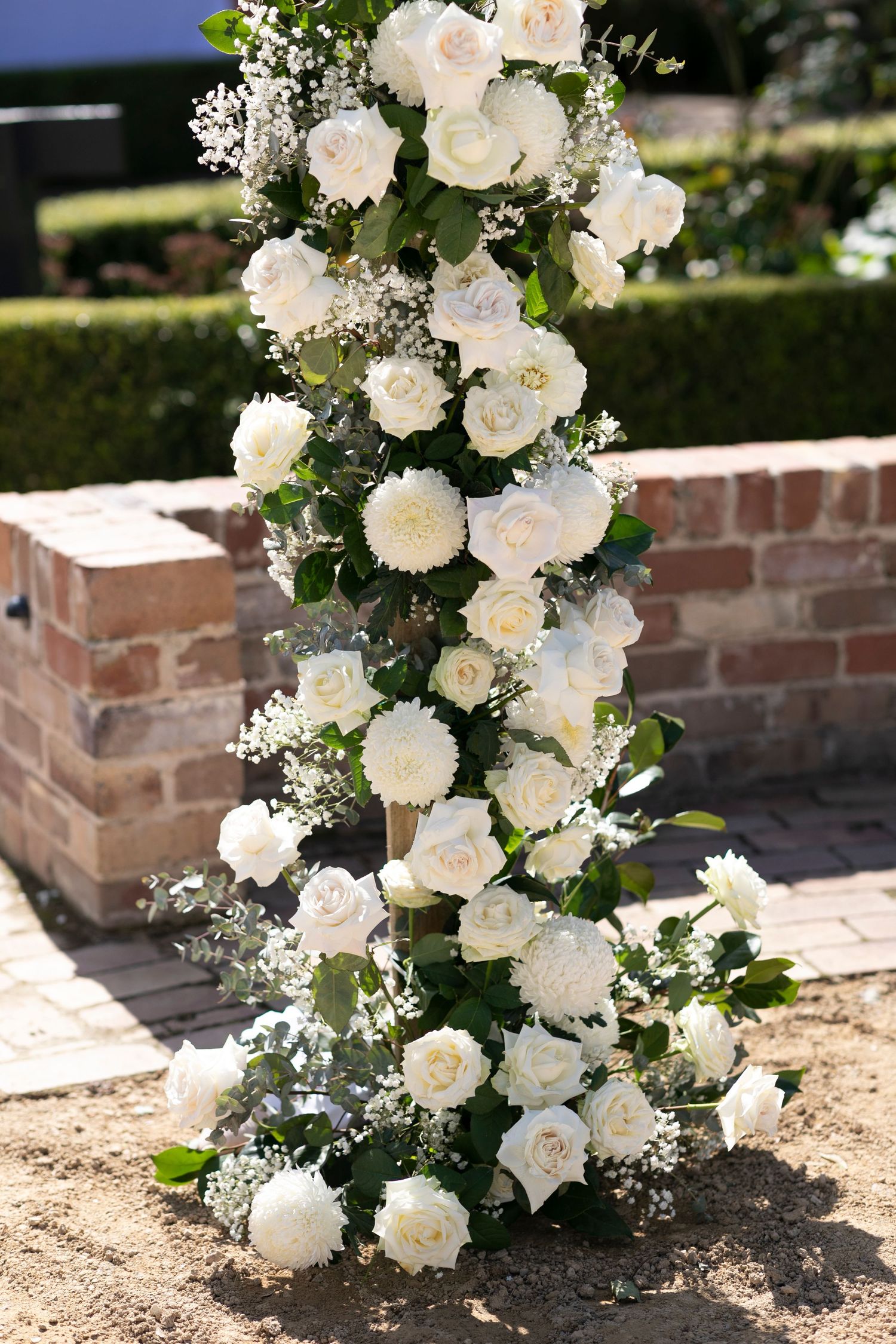 Elegant white rose and baby's breath floral arrangement cascading up a brick wall for a wedding ceremony.