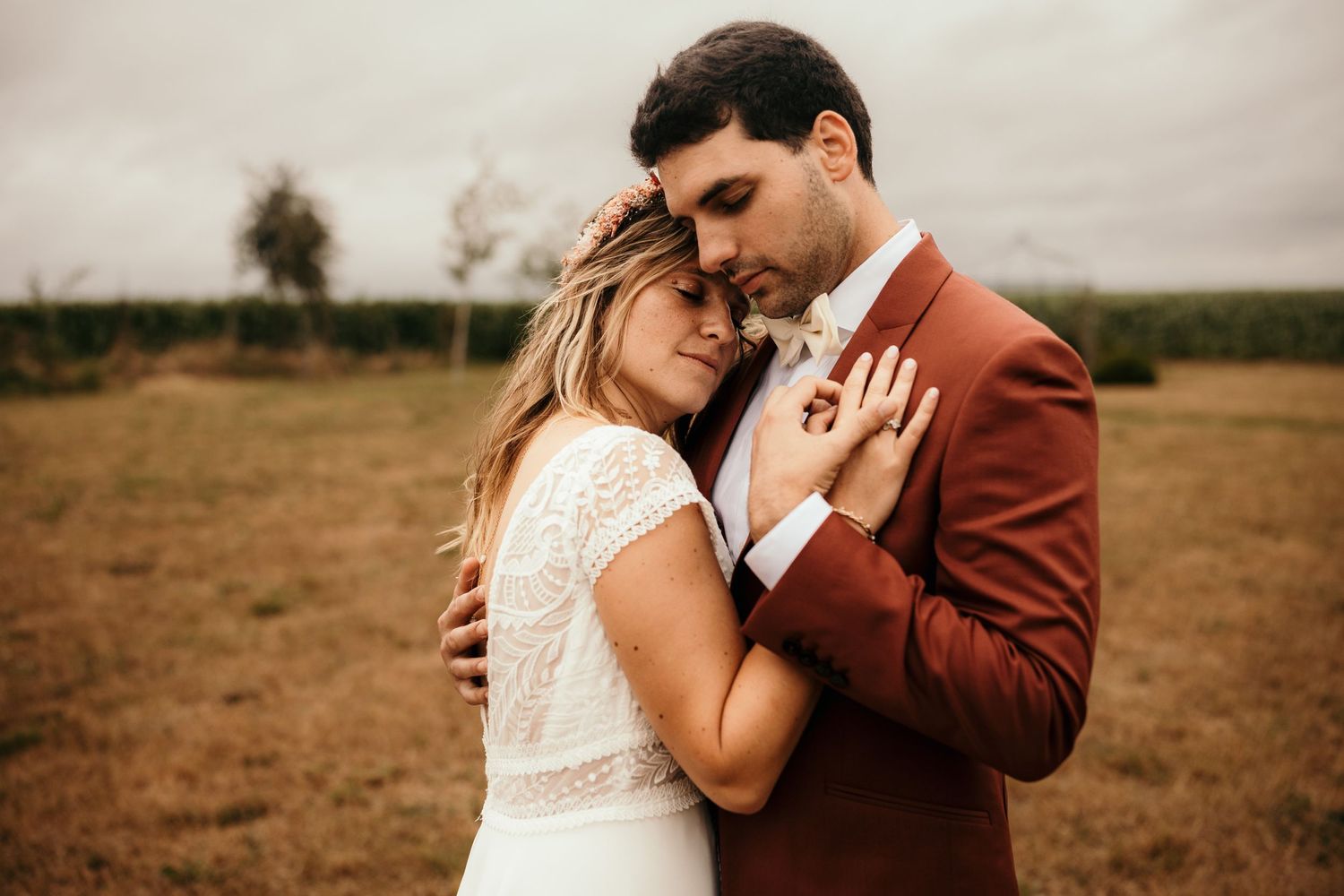 Intimate portrait of couple in rustic setting with rust-colored suit and lace dress.