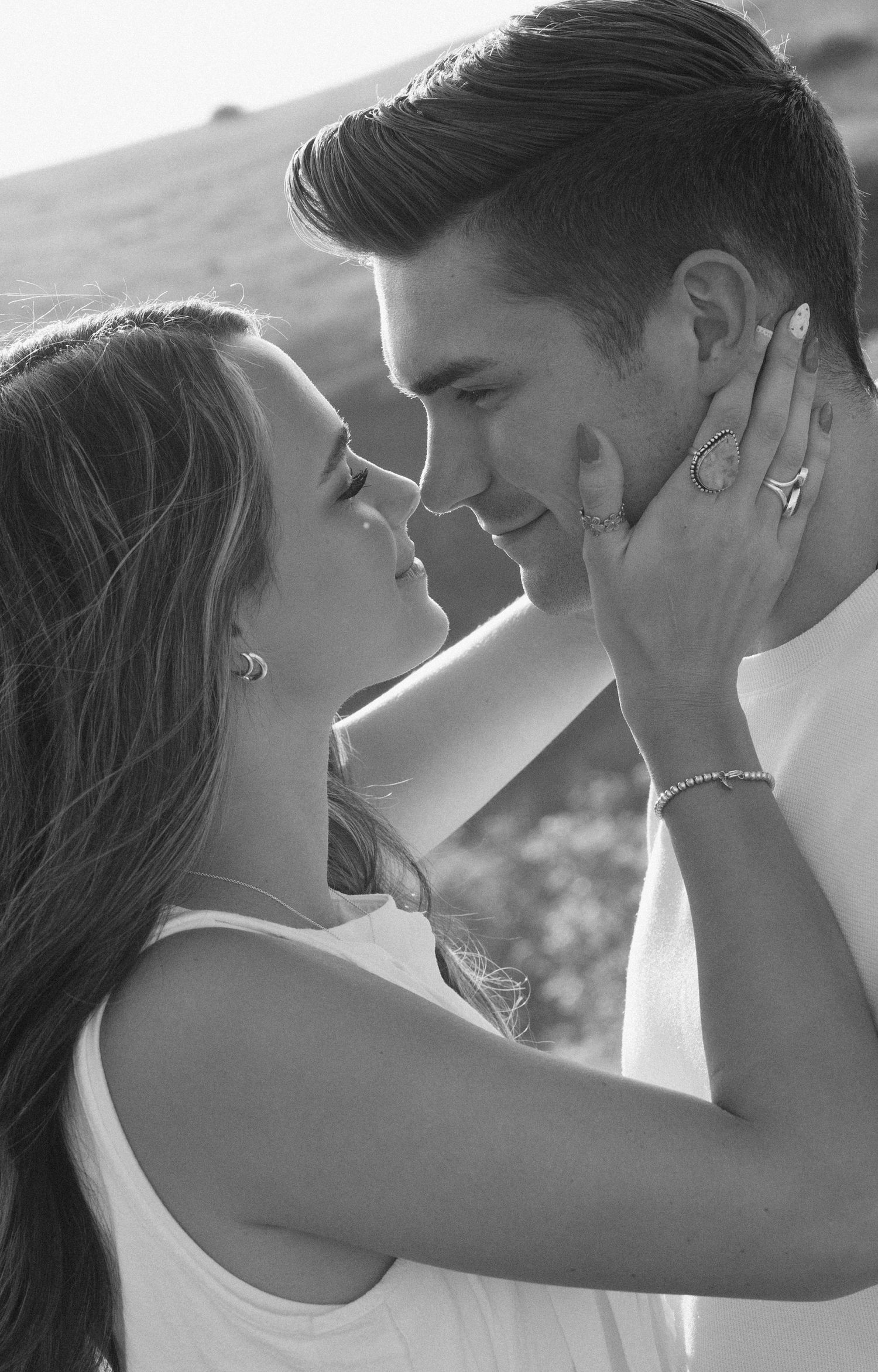 Romantic black and white portrait of a couple sharing an intimate moment in soft sunlight outdoors.