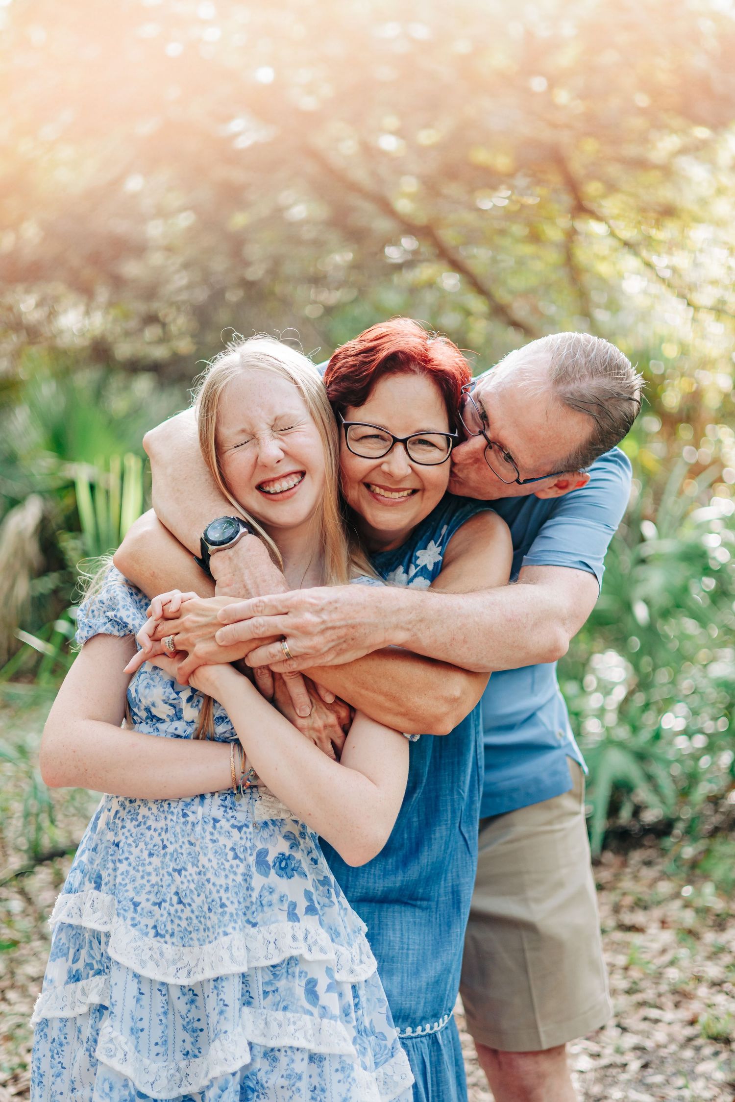Three people hugging and laughing together in a garden on a sunny day with beautiful natural lighting at Delray oaks nature trail.