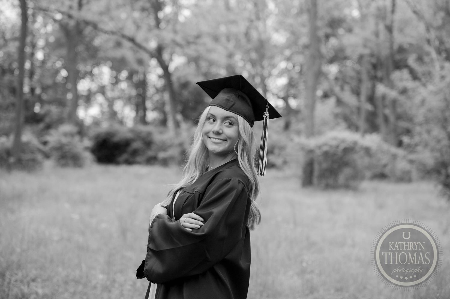 Two figures in graduation attire hug and celebrate outdoors in a wooded area during a post-graduation photoshoot.