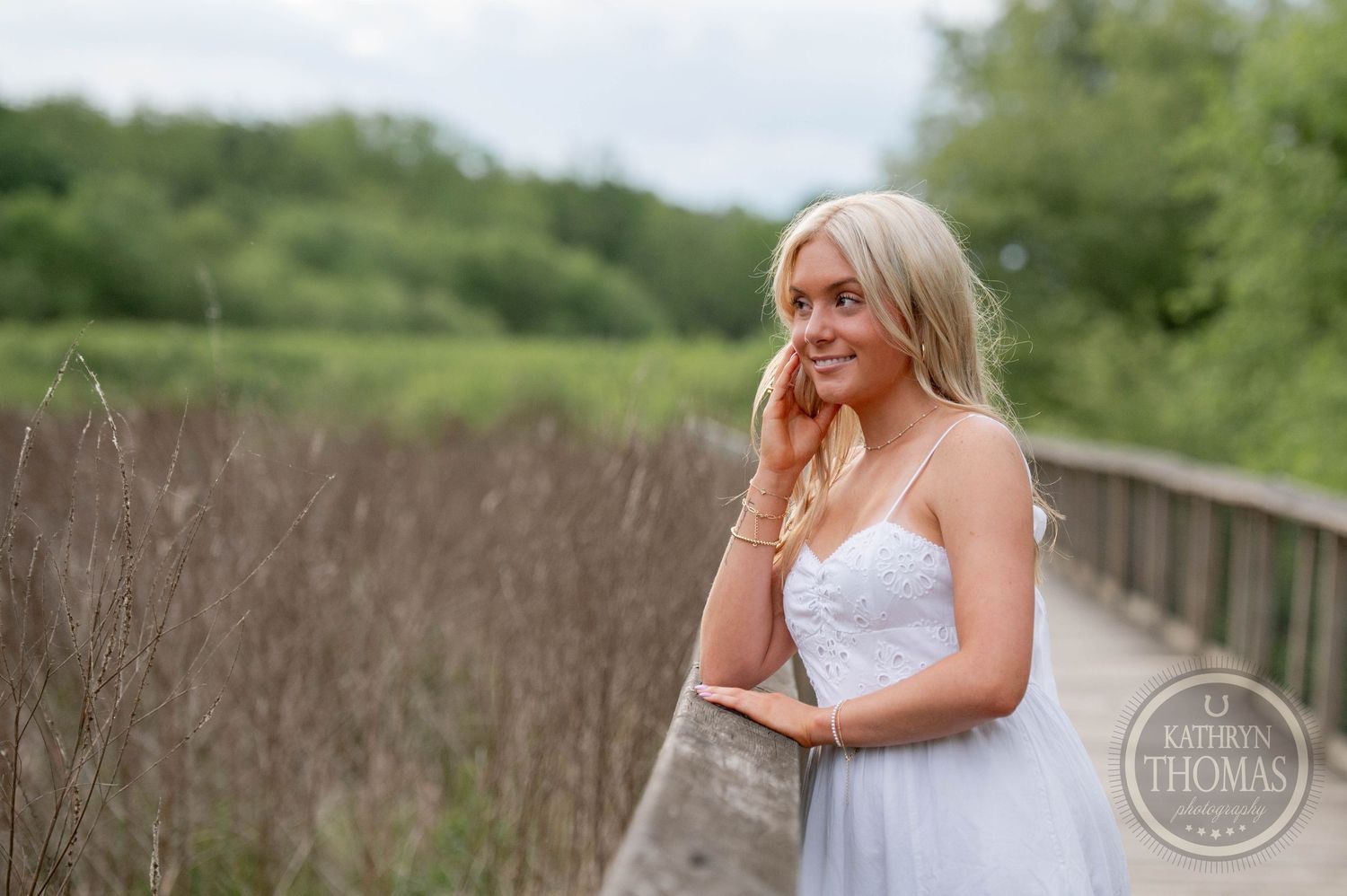 A flowing white sundress moves gracefully along a wooden boardwalk surrounded by lush summer greenery.