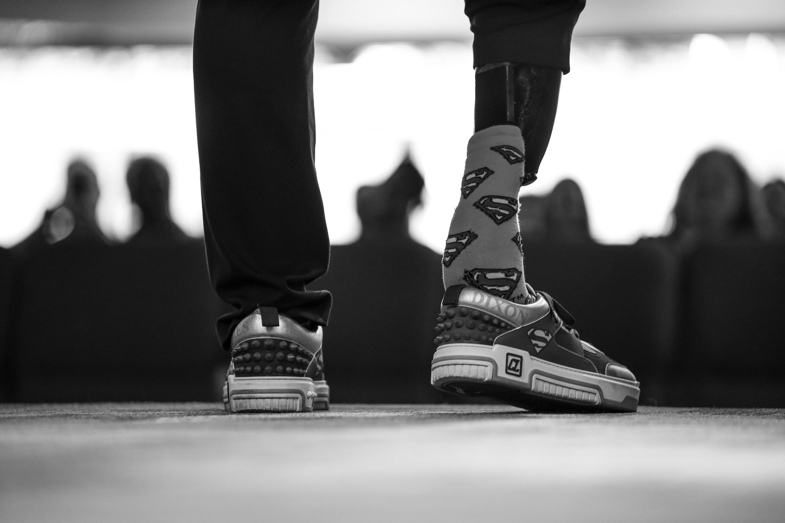Black and white photo of sneakers on stage with silhouetted audience members visible in the background.