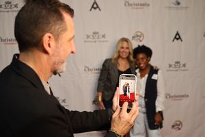Someone takes a photo with a phone at an event with sponsor logos visible on the backdrop wall.