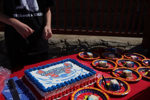 A decorated cake with blue icing and colorful paper plates arranged on a red tablecloth.