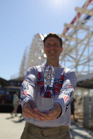 A commemorative medal or award being displayed against a roller coaster structure background.