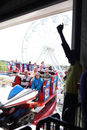 Amusement park visitors enjoy a thrill ride with a large Ferris wheel visible in the background.