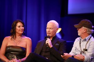 Three people sit on stage at a panel discussion with purple lighting and screens in the background.