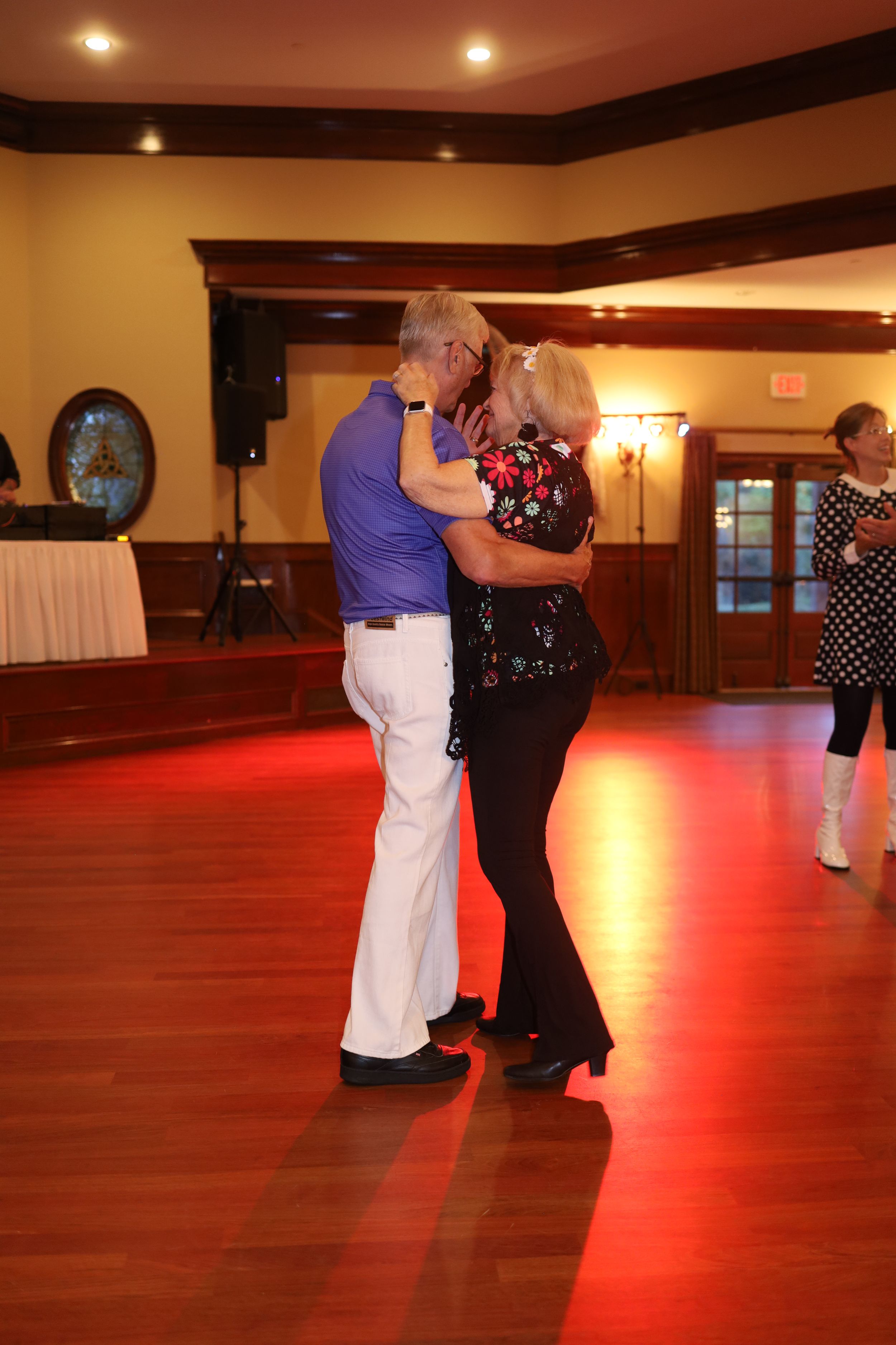 Two dancers move together on a polished wooden dance floor under warm lighting in an elegant ballroom.
