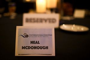A reserved place card showing 'Neal McDonough' name on a formal table setting with candlelight in the background.