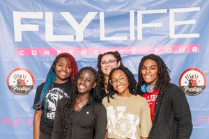 A group of people pose together for a photo in front of a pink and blue FLYLIFE promotional backdrop.