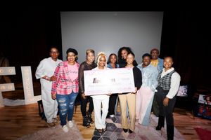 Group of people posing with large check on stage during an event presentation.