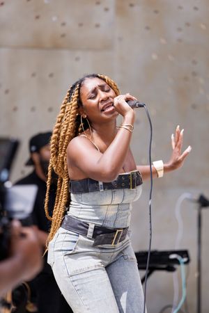 A performer in denim attire singing passionately on stage with long blonde braids.