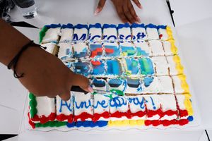 Hands cutting into decorated Microsoft-themed celebration cake with colorful frosting.