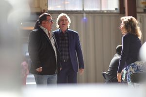 Three people having a conversation in casual attire while standing together indoors.