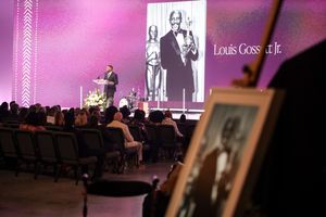 A person stands on stage during a presentation with a large projected black and white image displayed behind them.
