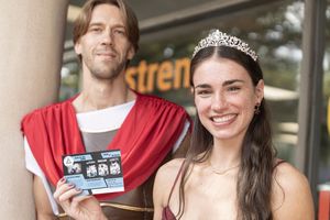 Customer wearing a tiara smiles in front of a grocery store entrance while holding a store card and shopping bag.