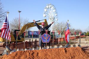 Construction equipment and American flags at an amusement park with Ferris wheel visible in the background.