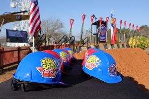 Blue construction hard hats with Fun Spot America logos sit on display against a background of American flags and dirt track.