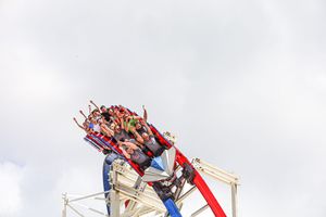 Red and white mechanical carnival ride reaching up into cloudy sky at an amusement park.