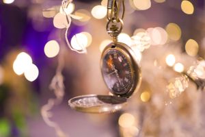 Vintage pocket watch hanging in front of blurred bokeh lights creating a dreamy atmosphere.