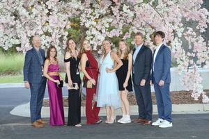 A group poses together in formal attire in front of a backdrop with beautiful pink cherry blossoms.