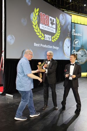 People interact on a dark stage with award graphics displayed on large screens in the background.