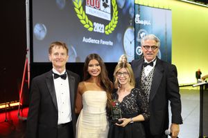 A group poses together at a formal awards ceremony with a projection screen visible in the background.